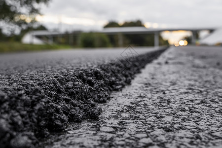行业之道一大层新鲜的热沥青 浅景深中的沥青原料层 滚子在新的道路上滚动新鲜的热沥青 道路建设 修建一条新路材料柏油石头路面粒状铺路路线机背景