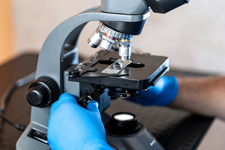 退伍老兵背景男性实验室助理通过显微镜检查生物材料样本 用蓝色橡胶手套调整显微镜拉紧手部的肌肉科学兽医医生细菌实验乐器镜片化学研究员护理背景