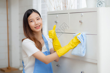 保活机制戴手套的年轻亚洲女性在房间里打扫卫生 管家用布料擦拭 女佣和服务 工人在客厅打磨灰尘 做家务和家务 生活方式概念青少年家庭管家保背景