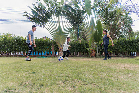 三人踢足球母亲 父亲和子女的女儿在自然外踢足球 野外一个园林公园闲暇微笑孩子游戏爸爸花园公园女孩孩子们父母背景