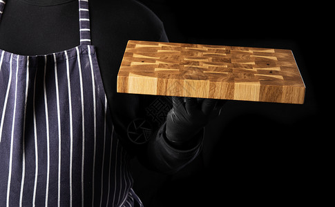 男黑衣服素材身穿条纹蓝色围裙和黑衣服的男厨师站立 手里握着一个长方形木制厨房切削板背景