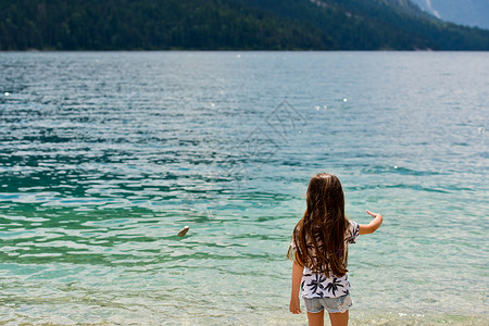 一个甜美的小黑发女孩站在奥地利的Plansee湖边 望着远处 从后面看 (笑声)背景图片