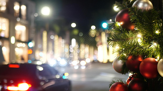 圣诞节素材车在模糊的闪闪发光的仙女背景上 用明亮的红球装饰的户外圣诞树的特写镜头 散焦花环灯散景效果 散焦的夜城街道 道路上有汽车火花夜生活背景