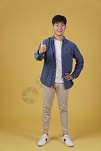 兴奋的随便的面带微笑 积极向上的亚洲年轻男子的肖像 穿着随意 大拇指竖起 赞同黄色背景中孤立的表情工作室拇指男人快乐男性手势学生背景