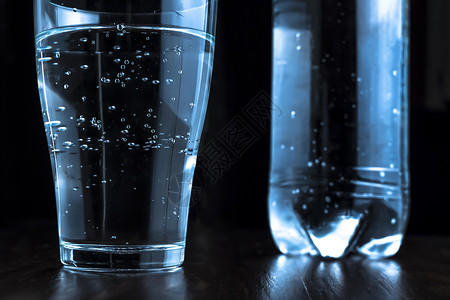 一杯苏打水或苏打水 深色背景中玻璃杯中的苏打矿泉水 背景是一瓶水 口渴 饮酒制度和平衡 健康的生活方式背景图片