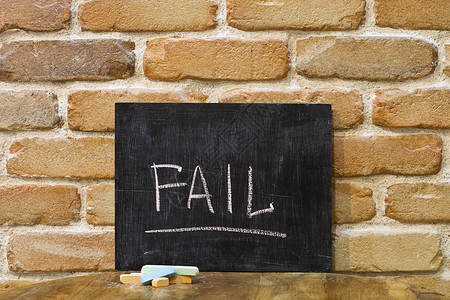 粉笔板上写着FAIL被亲手淹死的字眼和木桌上的粉笔 在砖墙背景上背景