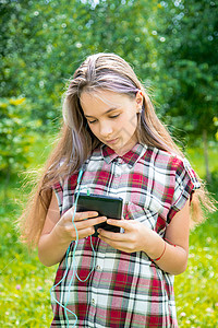 一名15岁的年轻女孩在公园的手机上读写讯息 在公园里使用手机背景图片