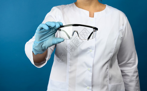 流行ps素材穿着白色医疗长袍的女医生站在蓝色背景上 佩戴保护性塑料眼镜(PS)背景