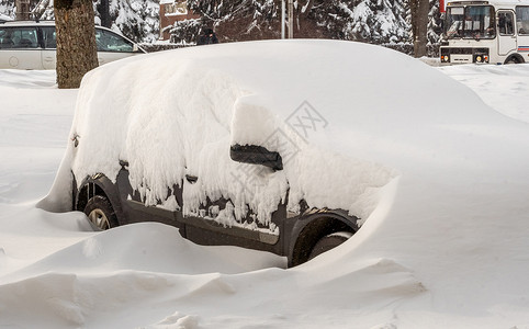 暴风雪过后的城市街道 汽车被困在冰雪之下 车辆被埋在路上的雪堆中 冬天大雪过后的停车场 未清洁的道路 破纪录的降雪量城市危险街道背景