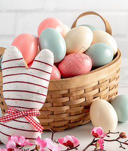 鸟巢里有粉红羽花的彩色复活节鸡蛋李子玩具庆典假期乐趣蓝色兔子篮子乡村木头背景图片
