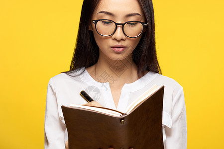 手持笔记本 学习学生黄色背景的亚洲女性快乐眼镜青少年知识眼睛青年办公室考试图书馆工人背景图片