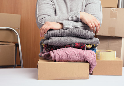 捐衣服身穿灰色毛衣的妇女把衣服包装在盒子里 援助和志愿的概念 搬家背景