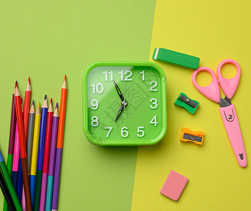 方形钟方形绿色时钟和绿色背景上的一叠多色木铅笔 顶视图背景