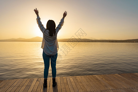 打码透明素材穿着透明衬衫的黑发女孩站在码头上 张开双臂望向天空 看着地平线 夕阳映照在海水上 从后面看的轮廓 沉思的概念背景
