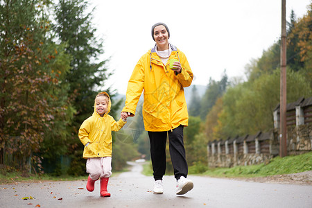 穿着雨衣的女孩母亲和女儿在雨后行走时穿着黄色雨衣的黄雨衣下雨农村家庭人行道女士女性季节童年木乃伊生活方式背景