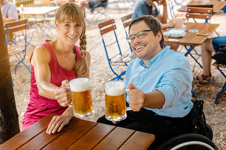 坐在轮椅上的残疾人和朋友喝啤酒朋友们啤酒乐趣帮助坐椅玻璃城市夫妻人士残障背景图片