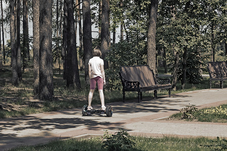 吸湿女孩骑着自行平衡的摩托车在公园里骑着树木力量运输电池均衡娱乐发动机横杆胡同马达背景