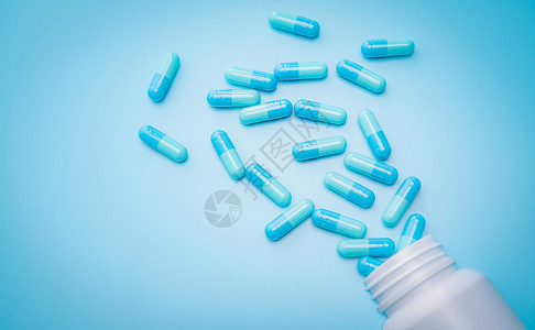 蓝色抗生素胶囊药丸在蓝色背景下从塑料药瓶中散开 抗生素耐药性 抗菌药物滥用 处方药 医药行业 卫生预算背景