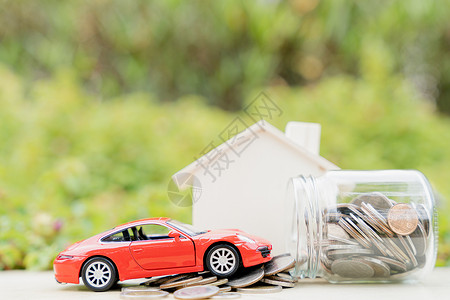 在模糊的绿色自然背景下 一罐硬币和一堆硬币上的红色汽车 存钱和投资概念小猪高清图片素材