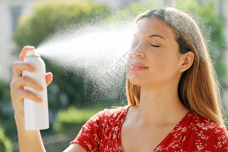 年轻女子在室外的脸上涂抹热水 用于护肤 定妆 帮助皮肤刺激 发红和蚊虫叮咬的温泉水背景图片