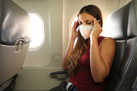 晕车COVID-19 戴 KN95 FFP2 面具的年轻女性在飞机上感觉不适 害怕在飞机上飞行的女人 大流行期间飞机上的压力 头痛背景