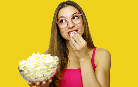 吃爆米花的快乐开朗的女人在黄色背景下看着一边 女孩拿着大玻璃碗 里面放着电影院的爆米花头发工作室闲暇食物女士电影黑发女性拉丁情感背景图片