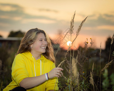 长草表情一个年轻女孩坐在草地上 在日落的光线下 长着高青草背景