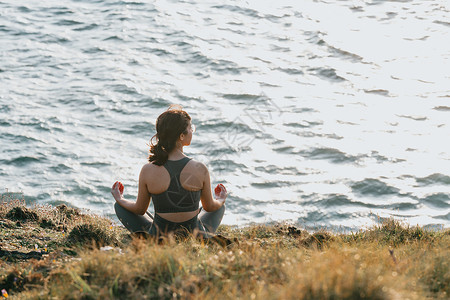 爱播洒人间在野外海岸的岩石上做瑜伽 阳光明媚的一天 海面在前方 空间放松与和平的概念复制人间休息运动姿势健康幸福太阳女性身体练习冥想成人背景