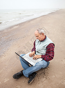 在海滩上拿着笔记本的老头工人互联网在线人士商务生活工作电脑公室自由职业者背景图片