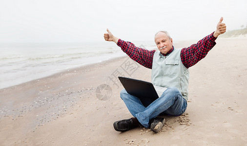 在海滩上拿着笔记本的老头男人闲暇公室老年自由职业者商业商务自由办公室工人背景图片