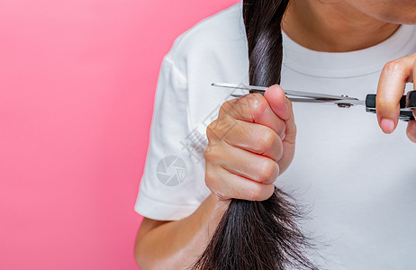 女性剪掉受损和干燥的头发 亚洲妇女用剪刀剪头发以捐赠给癌症患者 为乳腺癌患者捐赠头发 粉红色背景中留着黑色长发的女人背景