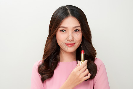 美丽的亚洲女人 拿着红口红口红并用背景图片