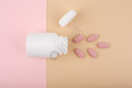 粉色药丸白色打开的药瓶 上面有粉色溢出的药丸 背景是柔和的粉色和米色背景