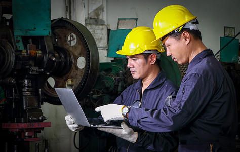 两名身着头盔制服的熟练亚洲工人正在使用计算机 笑声工程师领班导师药片检查员制造业控制机械仓库电脑背景图片