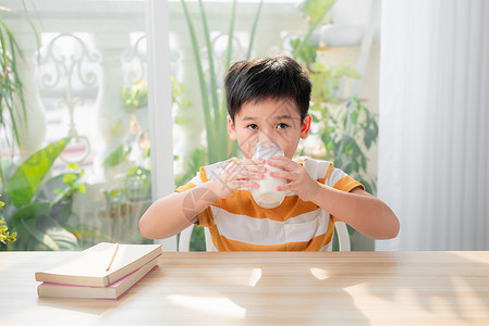 可爱男孩在做功课后坐在桌子上喝着牛奶的杯子家庭作业教育水果童年男生玻璃孩子学生课堂学校背景图片