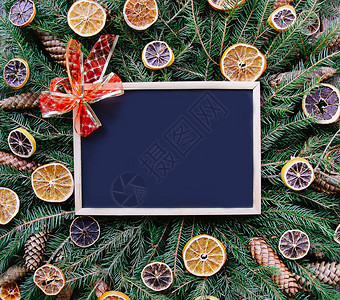 喜庆框圣诞节新年寒假作文 用干橙片和锥体装饰的绿色冷杉树枝上的空框板背景