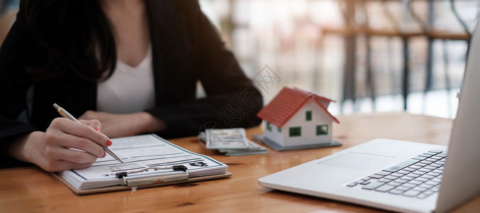 商业妇女签署租赁家庭文件并在木制办公桌上有一个房屋模型的近视女商务人士手金融高清图片素材