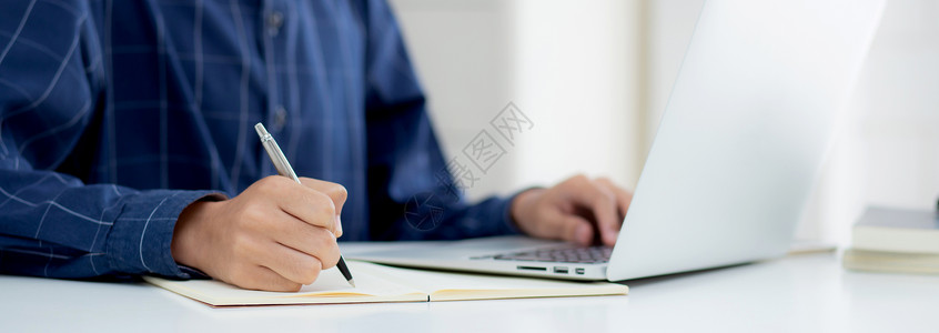 写博客的素材特写手的商务人士写在笔记上 同时在家里的办公桌上使用笔记本电脑 男性计划商业成功 作者和博客 在桌子上工作的商务人士 员工和工作背景