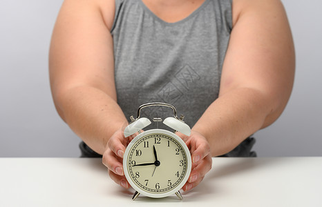妇女大胖子坐在一张桌子上 守着一个圆白闹钟 分数营养 减肥时间 坚持睡眠的概念背景图片