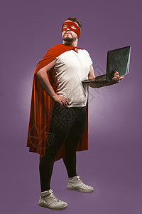 寻找超级免单王超级英雄男子拿着一台笔记本电脑仔细地寻找 身着红色超级英雄服装的商务人士 使用计算机在葡萄紫背景上摆姿势 快速互联网概念背景