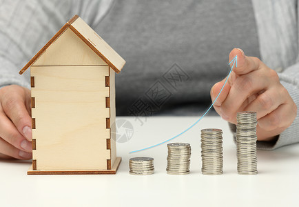 房子的木制模型 一堆硬币和一张上升图 男人坐在桌边 更高的房价 更高的租金和更高的抵押贷款利率背景图片