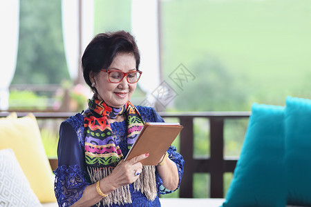 新加坡叻沙坐在沙发上 用平板电脑坐着的亚洲高级女性退休母亲媒体互联网技术旅行社交假期药片老年背景