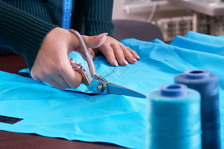 在裁缝制衣室 餐饮店 切割蓝布的服装师缝纫磁带衣服桌子测量织物剪裁剪刀工作室纺织品背景图片