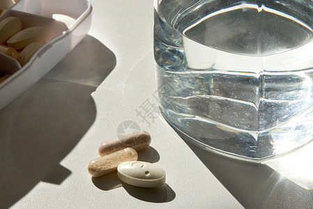 水毒白桌上的玻璃杯和药片处方药店科学疼痛疾病药品治疗医院胶囊玻璃背景