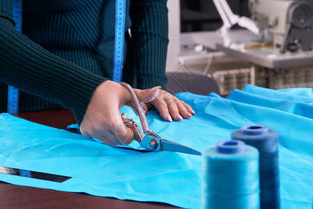 在裁缝制衣室 餐饮店 切割蓝布的服装师桌子剪刀维修设计师缝纫蓝色工艺衣服女士女裁缝背景图片