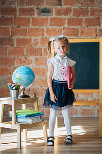 黑板视觉辅助身着校服的可爱小女孩 穿着校服 坐在有书本的校董会旁边背景