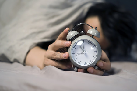 8小时睡眠毯子下面的年轻人手握着一个古老的闹钟快乐小时手表男生压力就寝枕头倒数睡眠时间背景