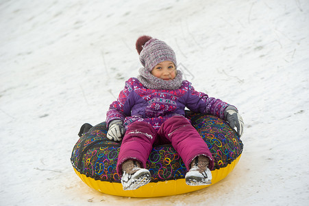 女孩看雪一个冬天的小女孩 穿着紫色衣服和一个充气圆圈 在街上的山下骑马游乐街道设施新年下坡雪花圣诞礼物孩子女孩帽子背景