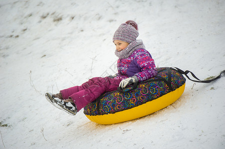 小充气的一个冬天的小女孩 穿着紫色衣服和一个充气圆圈 在街上的山下骑马孩子们小姑娘新年手套雪花帽子游戏微笑童年设施背景