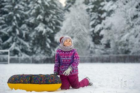 雪与小女孩一个冬天的小女孩 穿着紫色衣服和一个充气圈 在一片雪覆盖的森林里走在街上小姑娘孩子们雪花游戏圆圈童年孩子森林圣诞礼物微笑背景